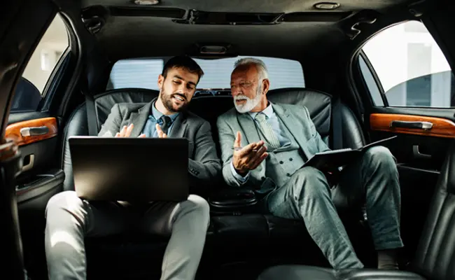 A picture op two customers in back seat of one of our luxury vehicles and seem relaxed, and enjoying the ride while working on their laptops.