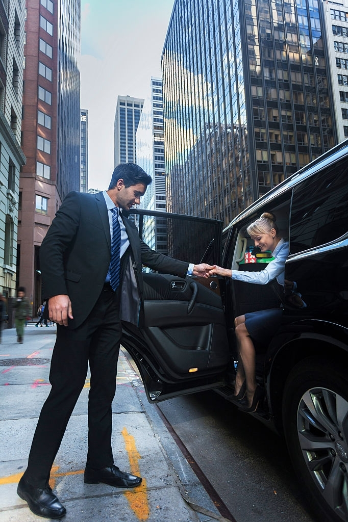 A picture of one of our chauffeurs dropping off a customer and helping her step out of the vehicle to the sidewalk