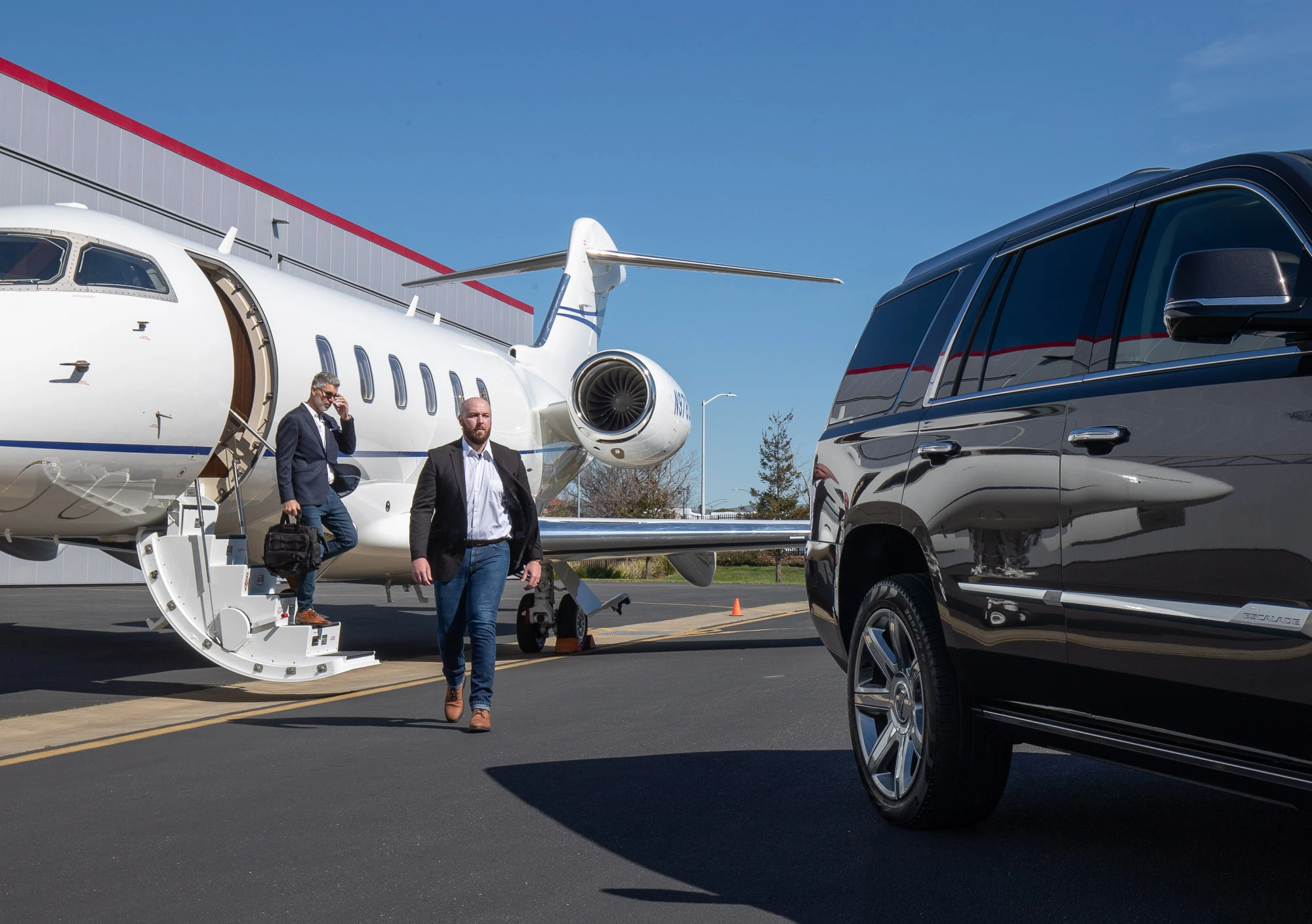 A picture of one of our luxury vehicles and out customer walking towards it from a private jet in an FBO facility private airport