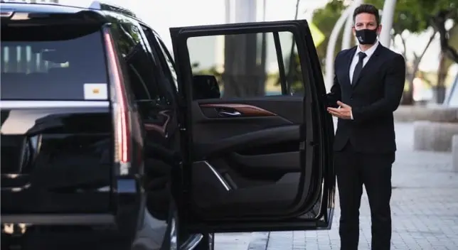 A picture of one of our chauffeur welcoming a customer and wearing a mask for their safety and opening the door for him